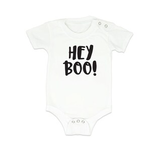 Può includere: Body bianco per neonato con maniche corte e testo nero che dice "Hey Boo!"