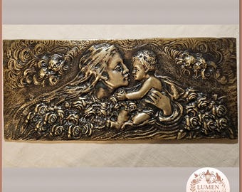 May include: A rectangular, bronze-colored relief sculpture depicting a mother and child. The mother, with flowing hair, holds the child, surrounded by roses and ornate details. The artwork has a classical, antique aesthetic.