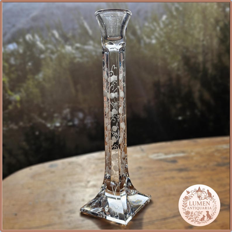 Pu&ograve; includere: Un candelabro di vetro trasparente con base quadrata e stelo alto e sottile. Lo stelo &egrave; decorato con un motivo floreale inciso. Il candelabro &egrave; progettato per contenere una singola candela.