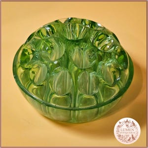 May include: A green glass bowl with a unique design. The bowl has a series of rounded, bubble-like shapes on the inside, creating a textured appearance. The bowl is likely vintage or antique, with a classic design.