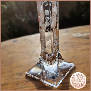 Pu&ograve; includere: Un vaso di vetro trasparente inciso, con base quadrata e corpo rettangolare alto. Il vaso presenta un delicato motivo floreale di cerchi e viticci. La base &egrave; larga circa 5 cm. Il vaso &egrave; probabilmente vintage o antico.