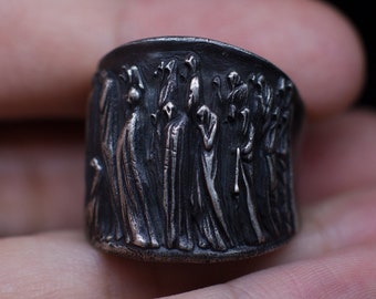 May include: A silver ring with a detailed design of a group of people standing in a line. The ring is worn on a finger.