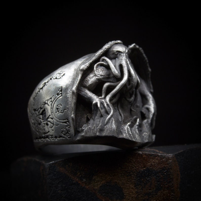 May include: A silver ring with a detailed design of a tentacled creature emerging from the water. The ring is engraved with intricate patterns.