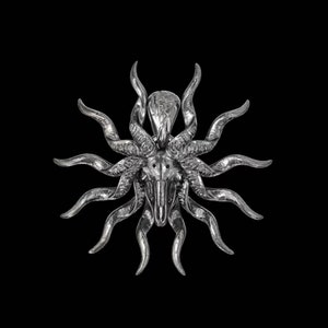 May include: A silver pendant in the shape of a skull with horns and rays emanating from the skull. The pendant is detailed and intricate.