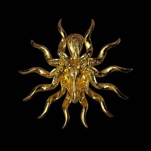 May include: A gold-colored, ornate, decorative skull with horns and rays emanating from the head. The skull is detailed and has a textured surface.