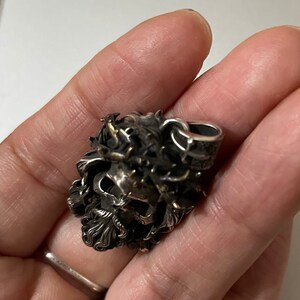 May include: A silver skull pendant with a crown of thorns and a beard. The pendant is detailed and intricate.