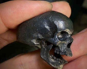 May include: A detailed silver skull ring with a textured finish. The skull is depicted with an open mouth and visible teeth.
