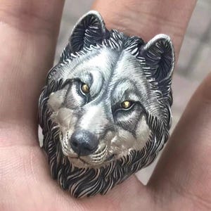 Op de afbeelding: Een zilveren ring met een gedetailleerd ontwerp van een wolfskop. De ogen van de wolf zijn geaccentueerd met gouden accenten.