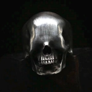 Peut inclure: Une bague en argent en forme de crâne avec une finition lisse et polie. Le crâne est représenté avec une bouche fermée et un design détaillé et réaliste.