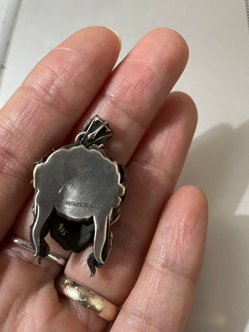 May include: Silver pendant with a detailed design, featuring the text "HAGER 2021" and the number "925" on the back.