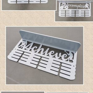 May include: White medal display rack with a shelf and 20 slots for medals. The rack features a cutout design with the word "Accomplish" and a figure of a person running.