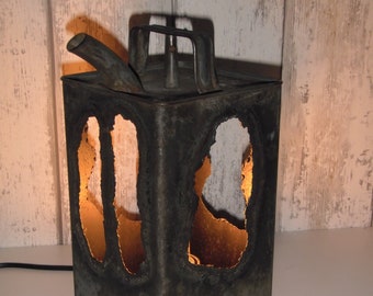 Könnte beinhalten: Eine einzigartige Lampe aus einem umgebauten Metall-Ölfass mit ausgeschnittenen Designs. Das Fass ist dunkelgrau mit einer rostigen Patina und hat einen Ausguss an der Seite. Die Lampe ist eingeschaltet und strahlt ein warmes Licht durch die Ausschnitte.