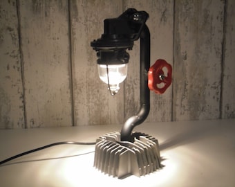 Könnte beinhalten: Eine schwarze Metalllampe mit einem klaren Glasschirm und einem roten Ventil. Die Lampe ist auf einem silbernen Motorblock montiert.