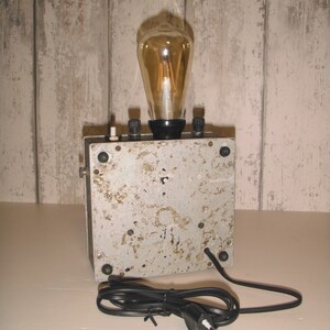 K&ouml;nnte beinhalten: Eine Lampe im Vintage-Stil mit einer klaren Gl&uuml;hbirne aus Glas und einem Metallsockel. Die Lampe hat ein Kabel mit einem Stecker mit zwei Stiften.