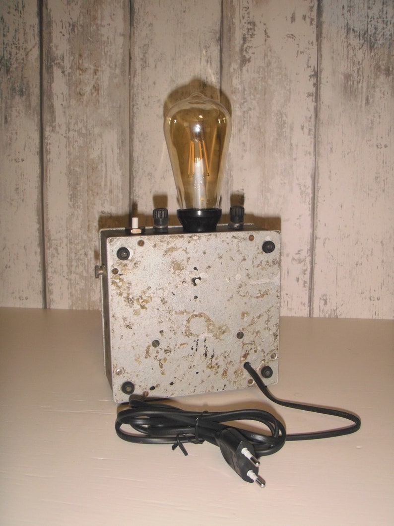 K&ouml;nnte beinhalten: Eine Lampe im Vintage-Stil mit einer klaren Gl&uuml;hbirne aus Glas und einem Metallsockel. Die Lampe hat ein Kabel mit einem Stecker mit zwei Stiften.
