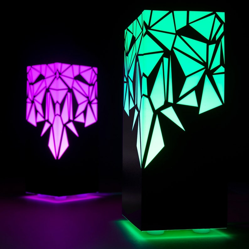 May include: Two black geometric lamps with colorful LED lights. The lamp on the left is lit with a purple and pink gradient, while the lamp on the right is lit with a green and blue gradient.