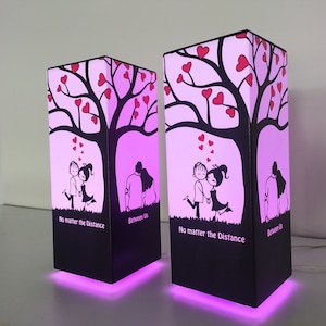 May include: Two pink and black table lamps with a silhouette of a couple under a tree with hearts. The text on the lamps reads "No matter the distance" and "Between Us".