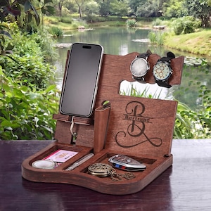 May include: A wooden desk organizer in a rich brown finish. It features a phone stand, watch holders, and compartments for small items like keys, a pen, and a wallet. The organizer is personalized with the name "Bertrand".