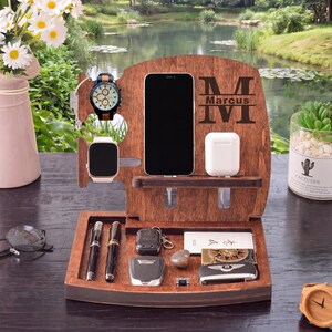 May include: A wooden charging station with spaces for a phone, watch, and earbuds. The station has a compartment for keys, pens, and other small items. The wood is a dark brown colour, and the name "Marcus" is engraved on the front.