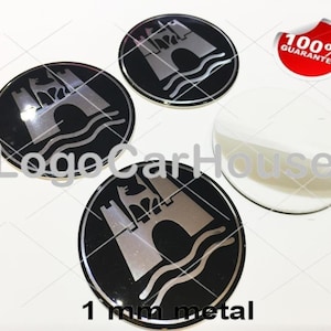 Könnte beinhalten: Drei kreisförmige schwarze und silberne Metallembleme mit einem Burg- und Wellenmotiv, begleitet von einer weißen Kleberückseite. Ein roter Aufkleber mit dem Text 100% GUARANTEE ist sichtbar, sowie LogoCarHouse und 1 mm metal.