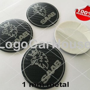 Könnte beinhalten: Drei schwarze und silberne Autoembleme mit einem stilisierten Vogel und dem Wort "SAAB" auf jedem. Die Embleme sind 1 mm Metall und haben ein Karbonfaser-Muster.