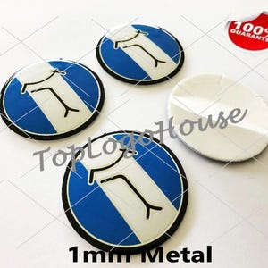 Può includere: Tre emblemi metallici circolari con un design a strisce blu e bianche con una grafica nera stilizzata, accanto a un emblema che mostra il suo retro adesivo bianco. Il testo 1mm Metal è visibile in basso ed è presente un adesivo 100% Guarantee.