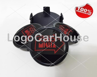 May include: Four black wheel center caps with a red "100% MIGA" logo. The caps are arranged in a circle with the logo facing outward.