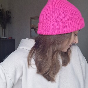 Op de afbeelding: Een felroze, geribbelde gebreide beanie. De hoed heeft een levendige fuchsia kleur en heeft een puntige bovenkant. De hoed is gemaakt van een dik, warm materiaal, perfect voor koud weer. De hoed is een stijlvol accessoire.