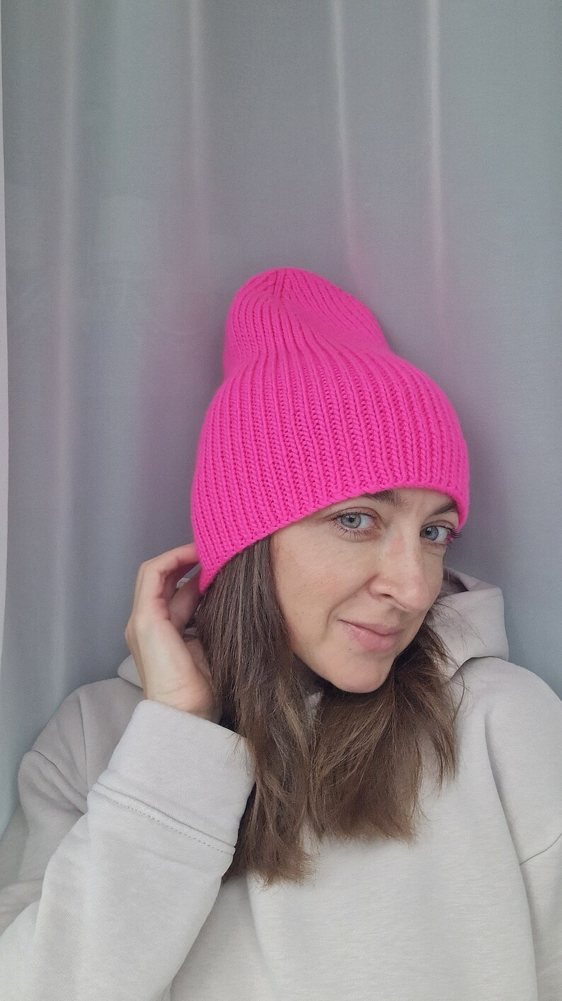 Op de afbeelding: Een felroze, geribbelde gebreide beanie. De hoed heeft een levendige, effen kleur en een klassieke, losse pasvorm. De hoed is gemaakt van een zacht, warm materiaal, ideaal voor koud weer.