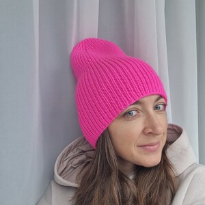 Op de afbeelding: Een felroze beanie-muts. De muts is gemaakt van geribbelde gebreide stof. De muts is effen van kleur en heeft een omgeslagen rand. Het is een winteraccessoire.