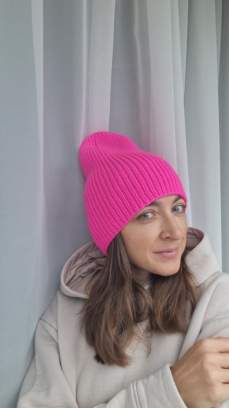 Op de afbeelding: Een felroze beanie-muts. De muts is gemaakt van geribbelde gebreide stof. De muts is effen van kleur en heeft een omgeslagen rand. Het is een winteraccessoire.
