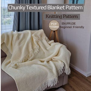 May include: A cream-colored, chunky textured blanket with fringe detail is draped over a sofa. The blanket has a waffle-like pattern. Text on the image reads "Chunky Textured Blanket Pattern" and "Knitting Pattern".