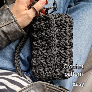 Könnte beinhalten: Eine schwarze gehäkelte Tasche mit einem silbernen Kettenriemen. Die Tasche wird von einer Person gehalten, die eine Jeansjacke und Jeans trägt. Der Text "Crochet pattern Easy" ist auf dem Bild zu sehen.