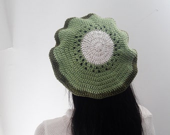 May include: A green and white crocheted beanie hat with a kiwi fruit design. The hat is being worn by a person with long black hair.