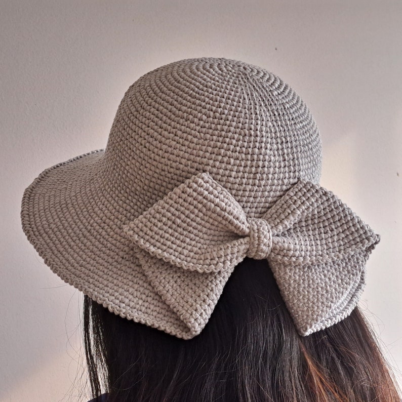 May include: A gray crocheted sun hat with a large bow in the back.