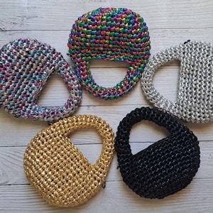 May include: Five crocheted handbags in different colours and patterns. The handbags are all small and have a round shape. The colours include silver, gold, black, rainbow, and a multi-coloured pattern.