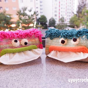 Peut inclure: Deux boîtes à mouchoirs crochetées à la main, l'une rose et l'autre bleue. Elles présentent de grands yeux globuleux, des bouches vertes et orange, et du papier de soie blanc. Les housses ont un design ludique, ressemblant à des monstres.
