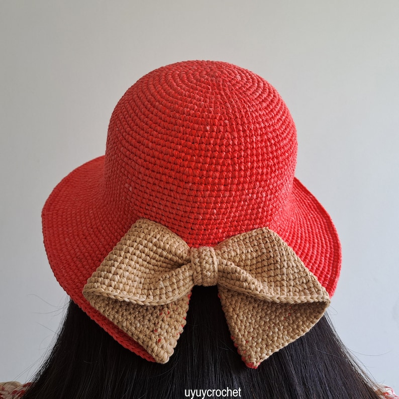 May include: A red crocheted sun hat with a large brown crocheted bow tied at the back.