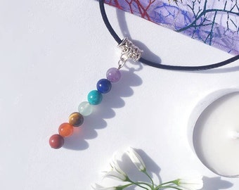 May include: A black cord necklace with a silver bead charm and a row of seven colorful gemstone beads. The beads are red, orange, yellow, green, blue, indigo, and violet.