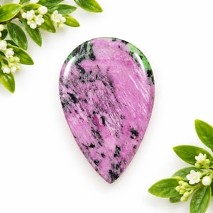 May include: A teardrop-shaped polished gemstone featuring a vibrant magenta and pink base color with prominent black mineral inclusions throughout the surface, displaying a smooth, reflective finish and a distinct natural crystalline texture.