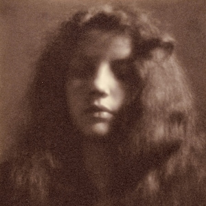 Könnte beinhalten: Sepiafarbenes Porträt einer Person mit langem, fließendem Haar. Das Gesicht des Subjekts ist sanft beleuchtet, mit Fokus auf Augen und Lippen. Das Bild hat eine Vintage- und künstlerische Qualität, die ein Gefühl von Nostalgie und Zeitlosigkeit hervorruft.