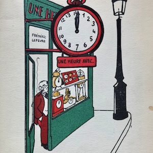 May include: A green storefront with a red clock above the entrance. The clock face reads "UNE HEURE AVEC..." and has a black hand pointing to the 12. The storefront has a sign that reads "UNE HEURE" and "FREDERIC LEFEVRE". There is a black street lamp to the right of the storefront.