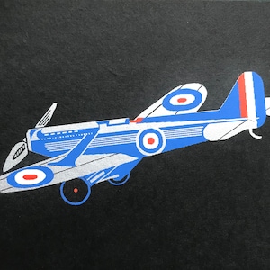 AVIÓN DE HÉLICE DE 1934 SERIGRAFÍA Impresión en cartulina negra 'Dignity' de Apsley Mills Tamaño de la imagen aprox. 5,5 x 3 pulgadas con borde en tinta plateada Escarapelas de la R.A.F.