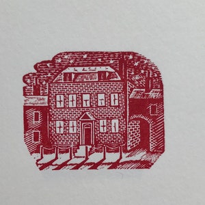 May include: A red woodcut illustration of a brick building with a door and windows. The building is surrounded by a fence and there are trees in the background.