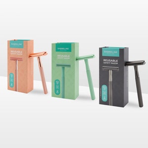 May include: Four boxes of reusable safety razors with different coloured handles. The boxes are green, black, pink, and blue. The razors are all the same design, but the handles are different colours. The boxes have the text "Shoreline" and "Reusable Safety Razor" on them.