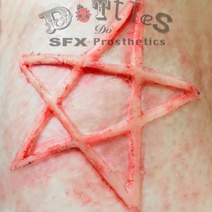 May include: A close-up of a prosthetic star-shaped wound with red coloring and a textured surface. The image includes the text "Dotties Do SFX Prosthetics" in the upper left corner.