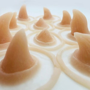 Pode incluir: Close-up de uma coleção de objetos em forma de cone castanho-claro dispostos em um padrão circular. Cada cone eleva-se de uma base branca com detalhes de anéis concêntricos, criando uma aparência texturizada e orgânica. O efeito geral lembra uma paisagem estilizada.