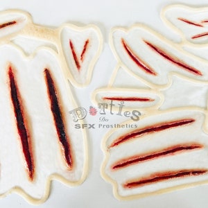 Pode incluir: Uma coleção de próteses de feridas SFX. As peças de látex apresentam feridas abertas de vários tamanhos com efeitos de sangue vermelho realistas. O texto "Dotties Do SFX Prosthetics" é visível.
