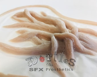 May include: A close-up of several pale pink, fleshy-looking prosthetics, possibly for special effects makeup. The pieces are arranged in a cluster, with a few extending outwards. The background is a white surface. The text "Dotties Do SFX Prosthetics" is visible.