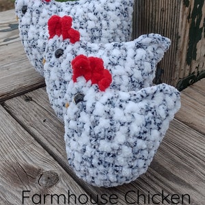May include: Three crocheted farmhouse chicken plushies in white and blue yarn with red combs. The plushies are sitting on a wooden surface. The text "Farmhouse Chicken PDF Pattern" is visible at the bottom of the image.